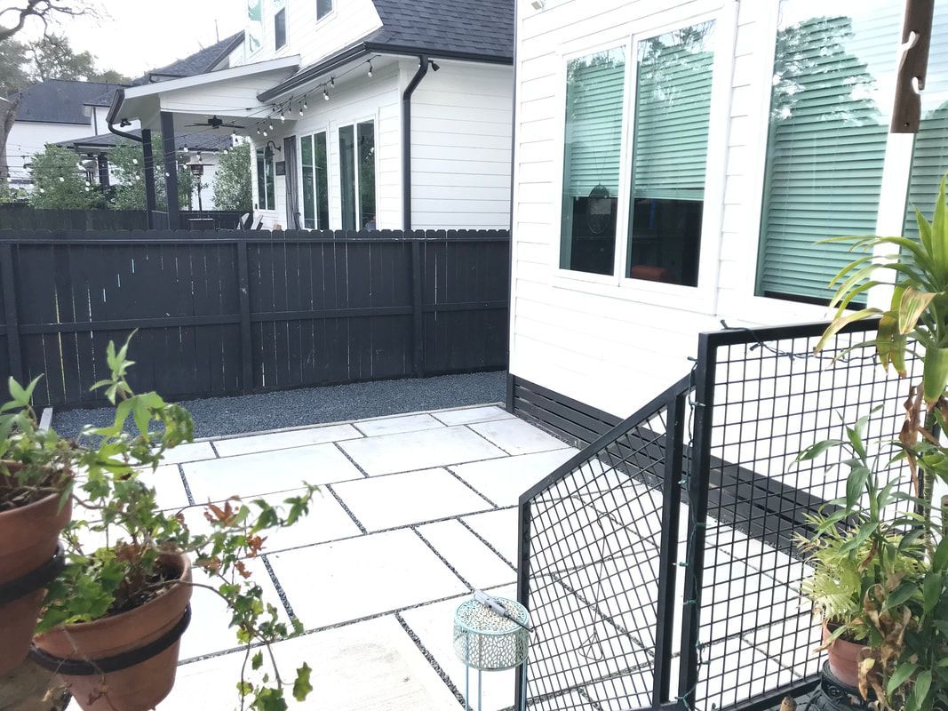 A black fence surrounds a patio in front of a white house.