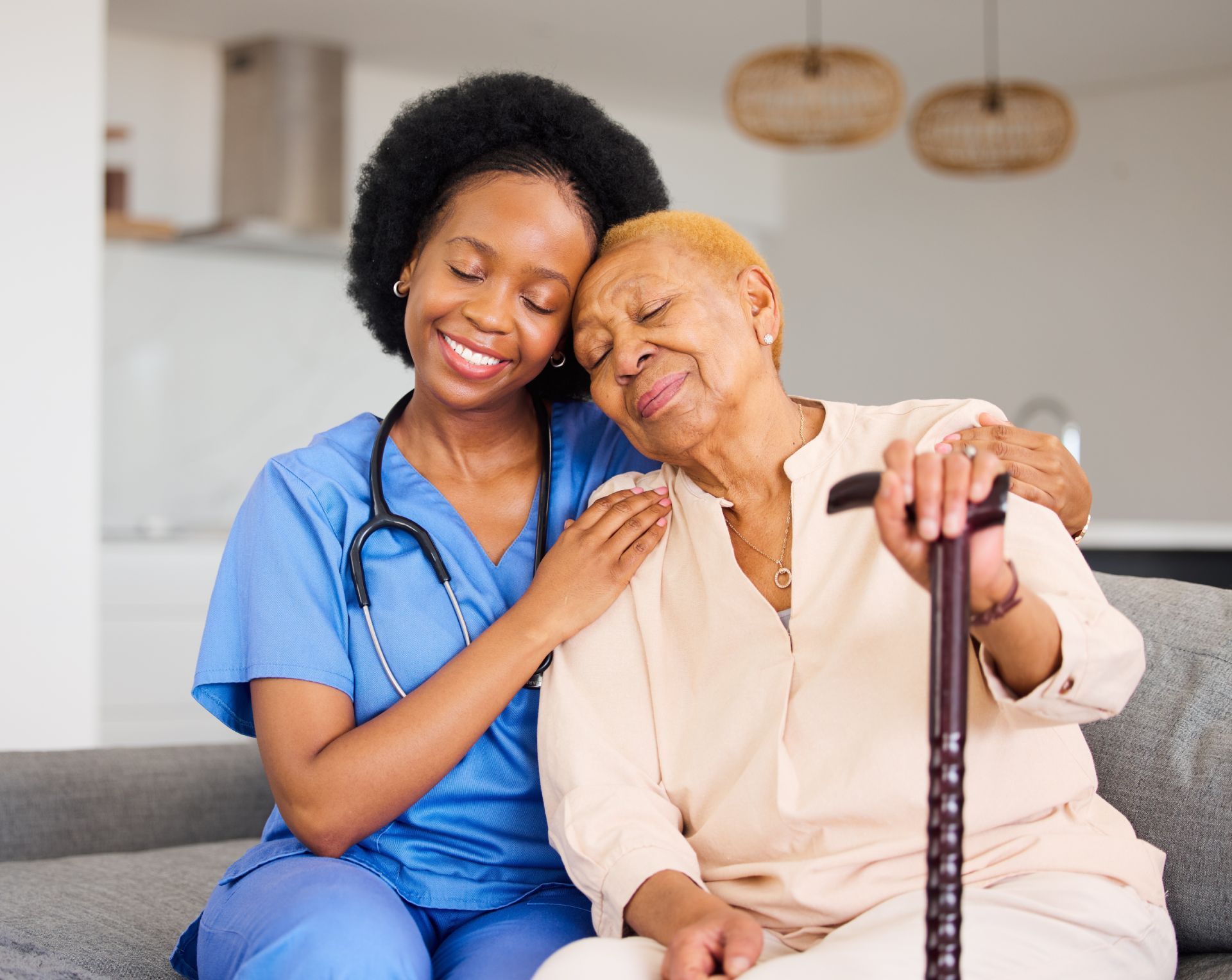 Caregiver and elderly person embrace; indoor setting, smiling faces, cane.