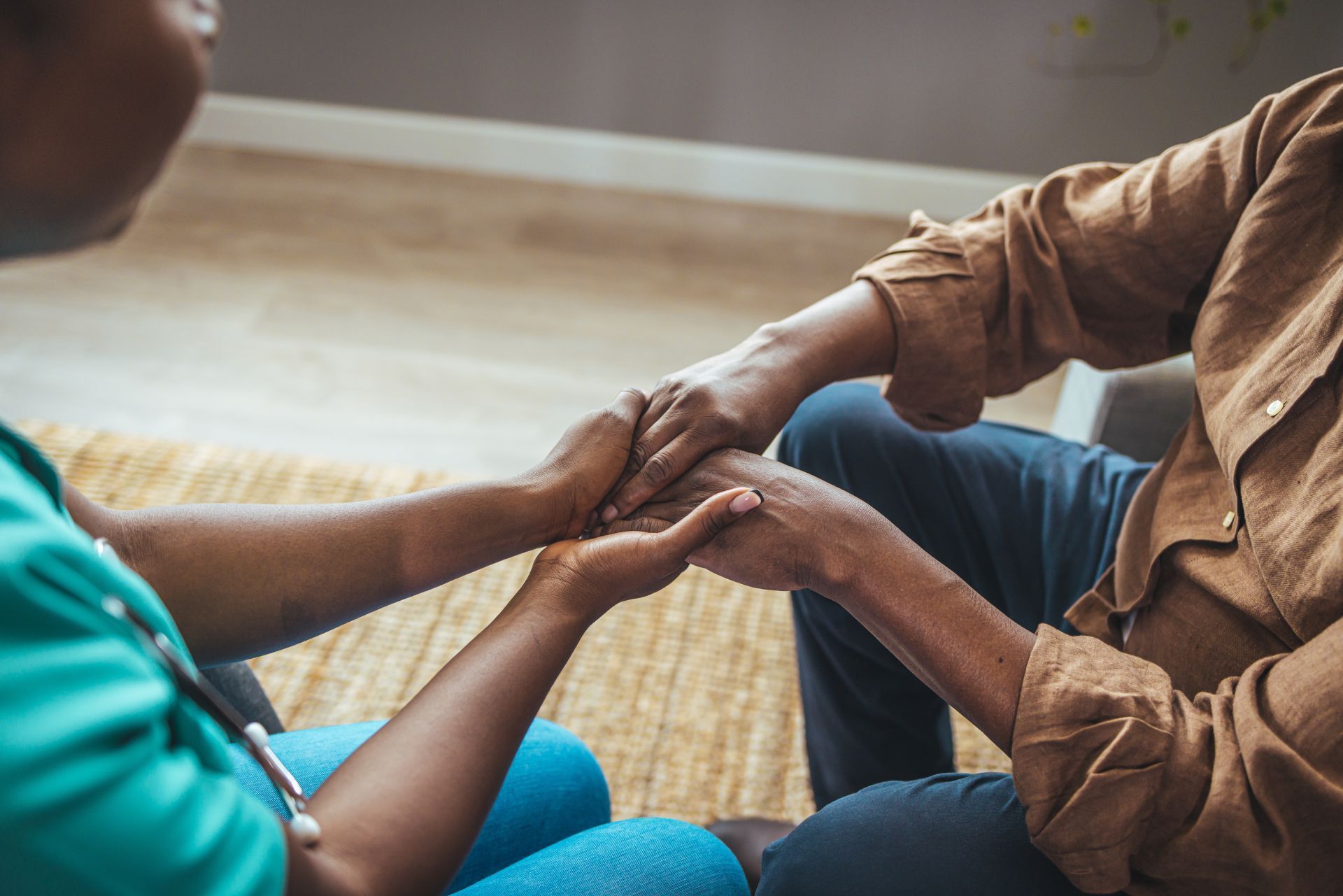 Person in brown shirt holding hands with person wearing a blue scrubs top.