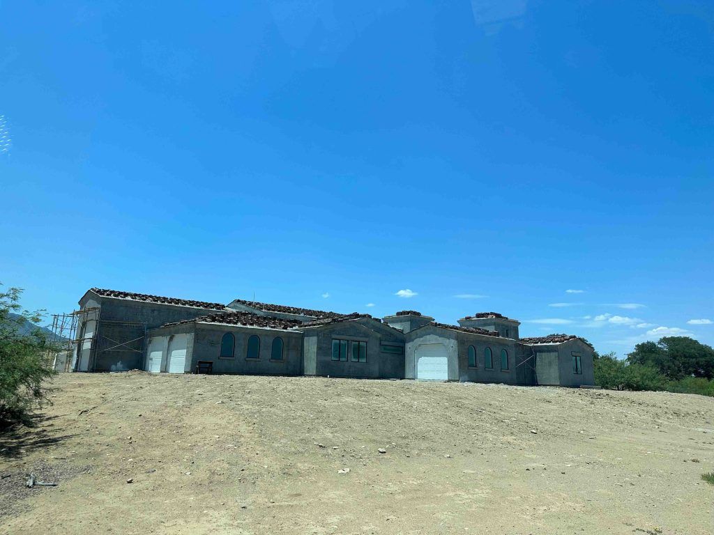 A large house is sitting in the middle of a dirt field.