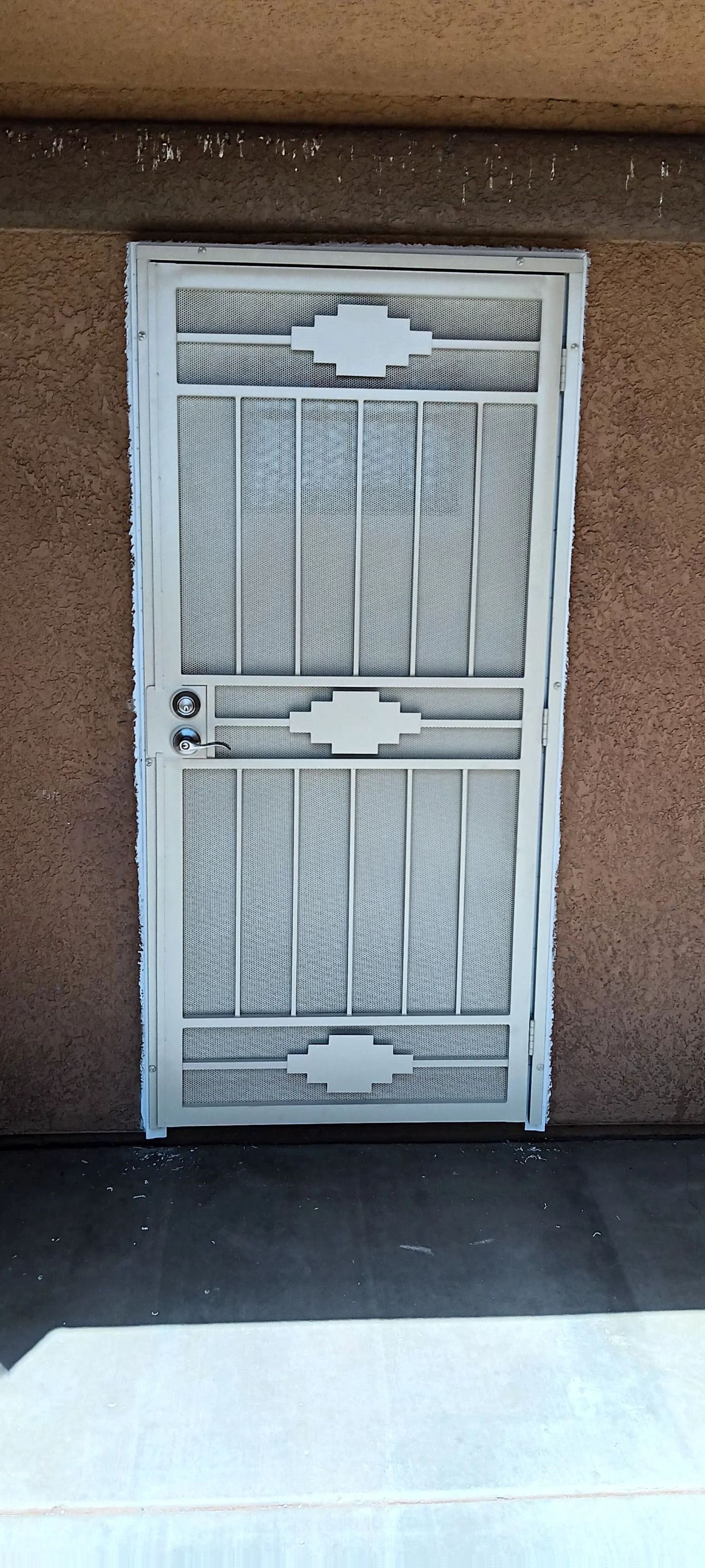 A white door with a wrought iron gate is on a brown wall.