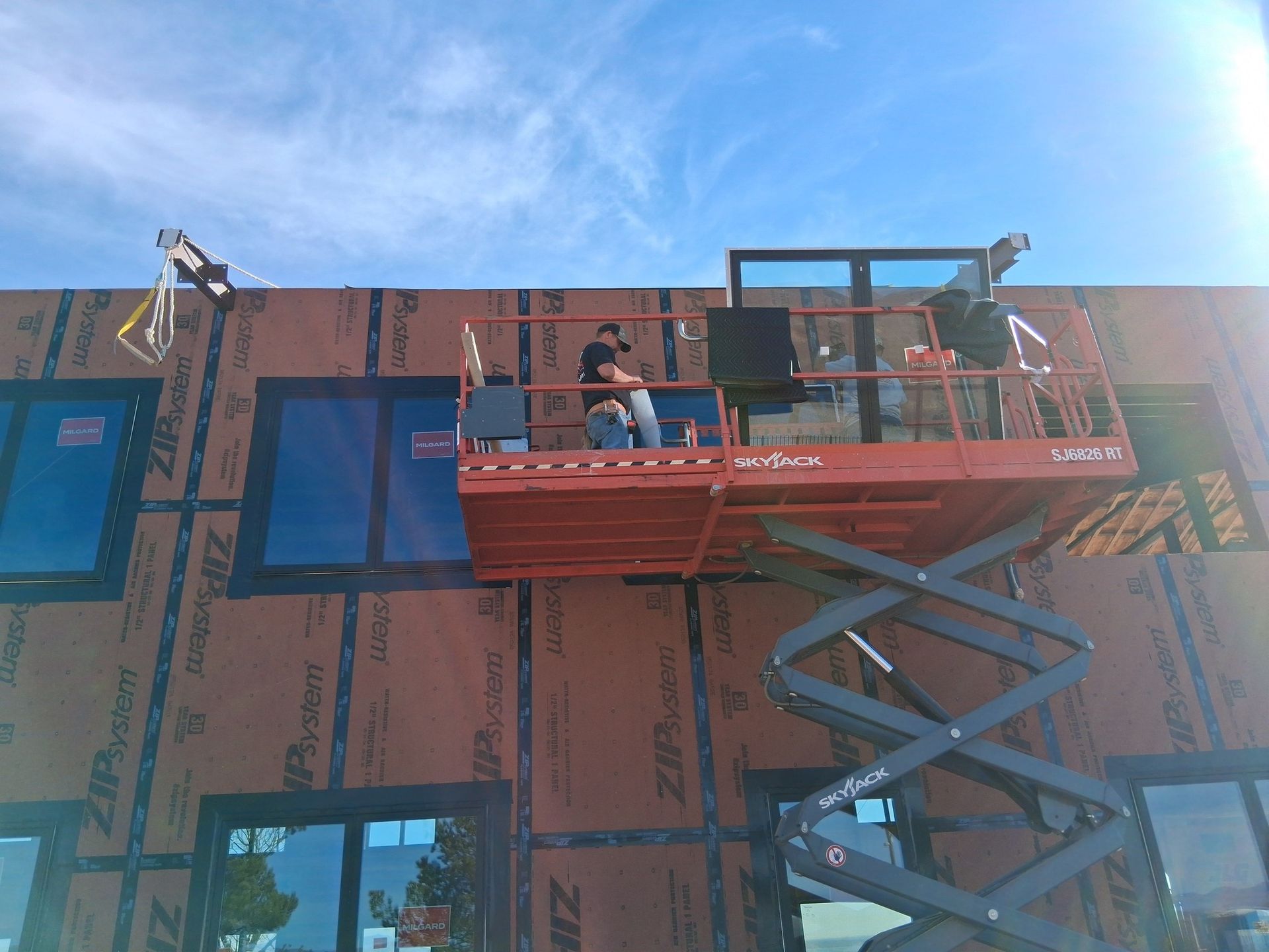A man is standing on a scissor lift on top of a building.