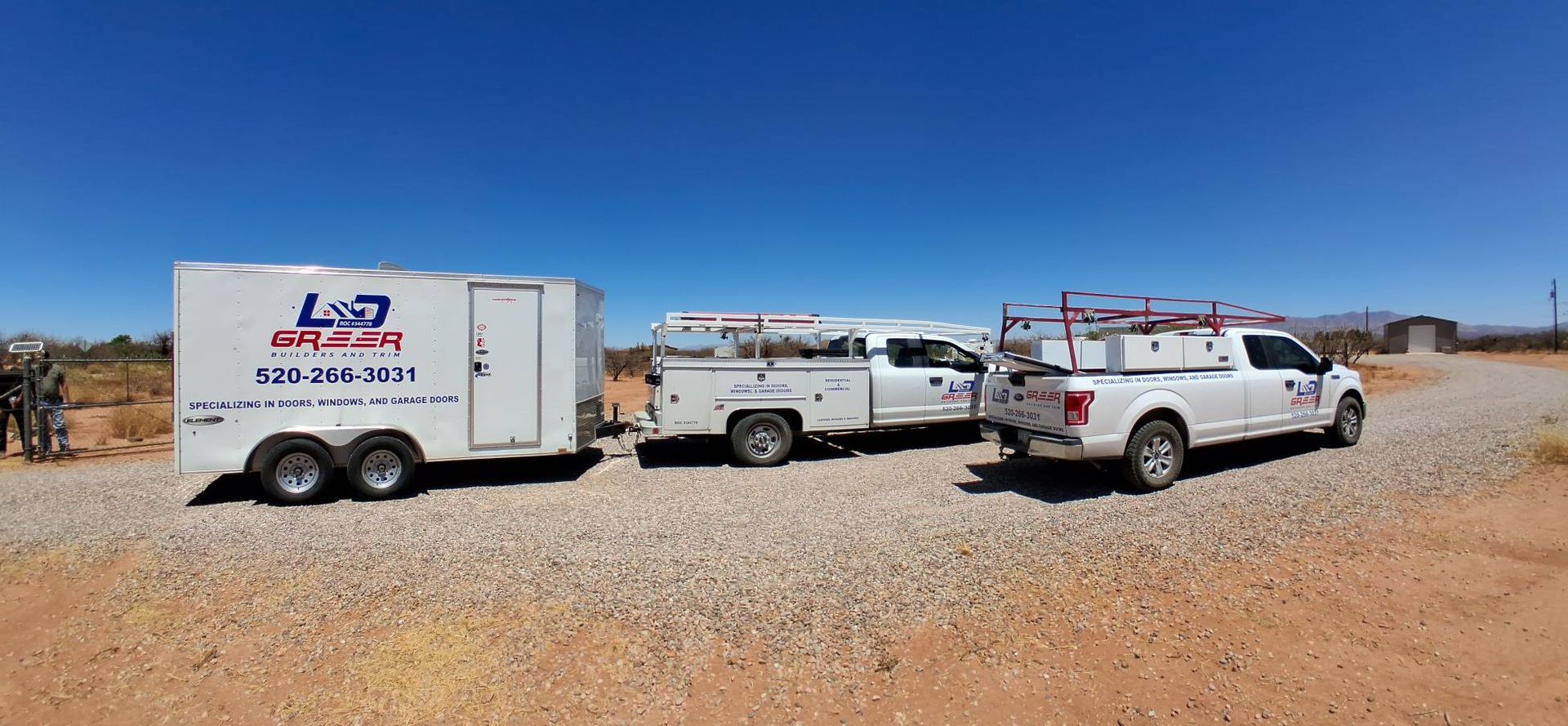 Three trucks and a trailer are parked on a gravel road.