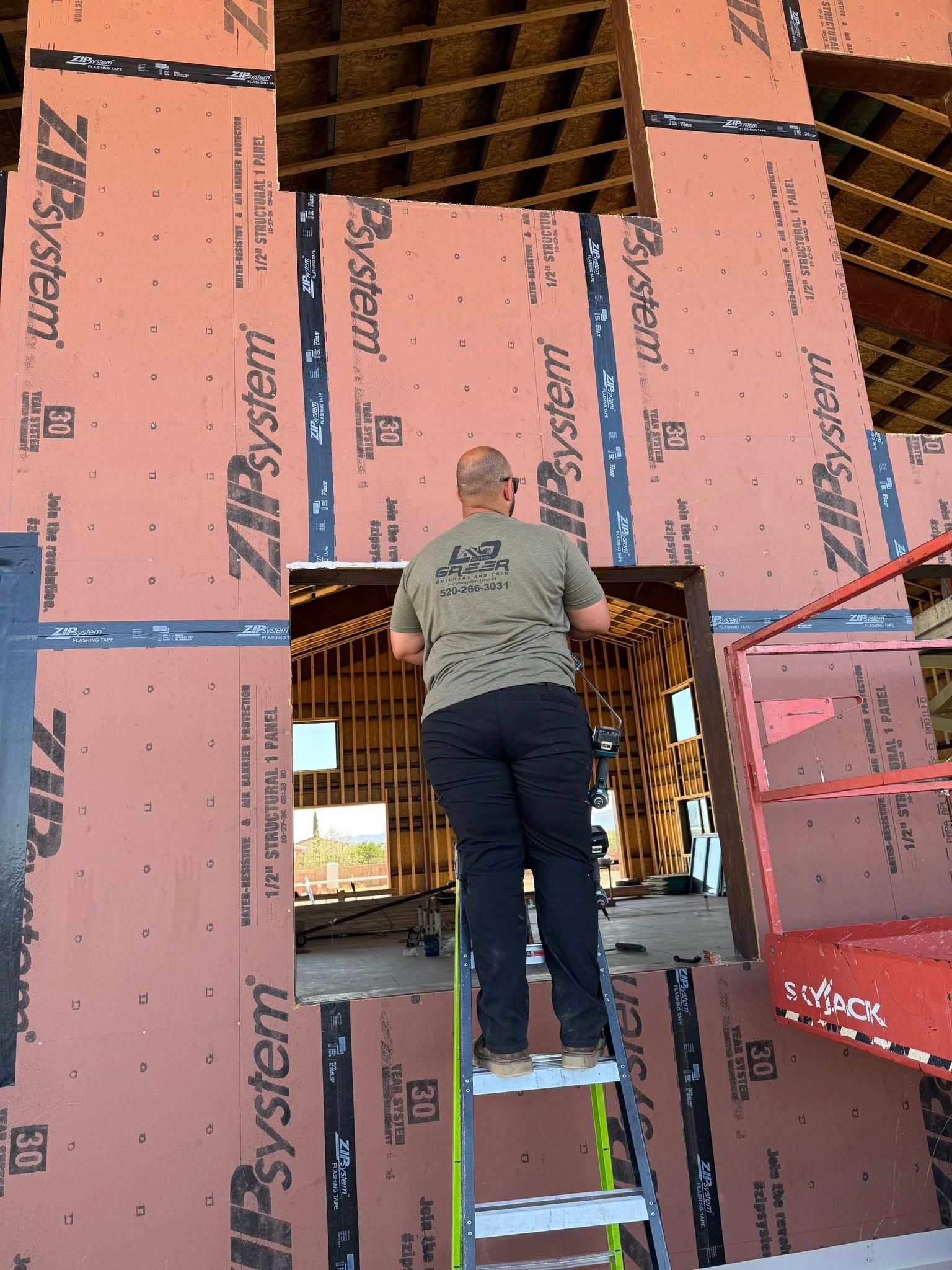 A man standing on a ladder in front of a wall of zip system boards