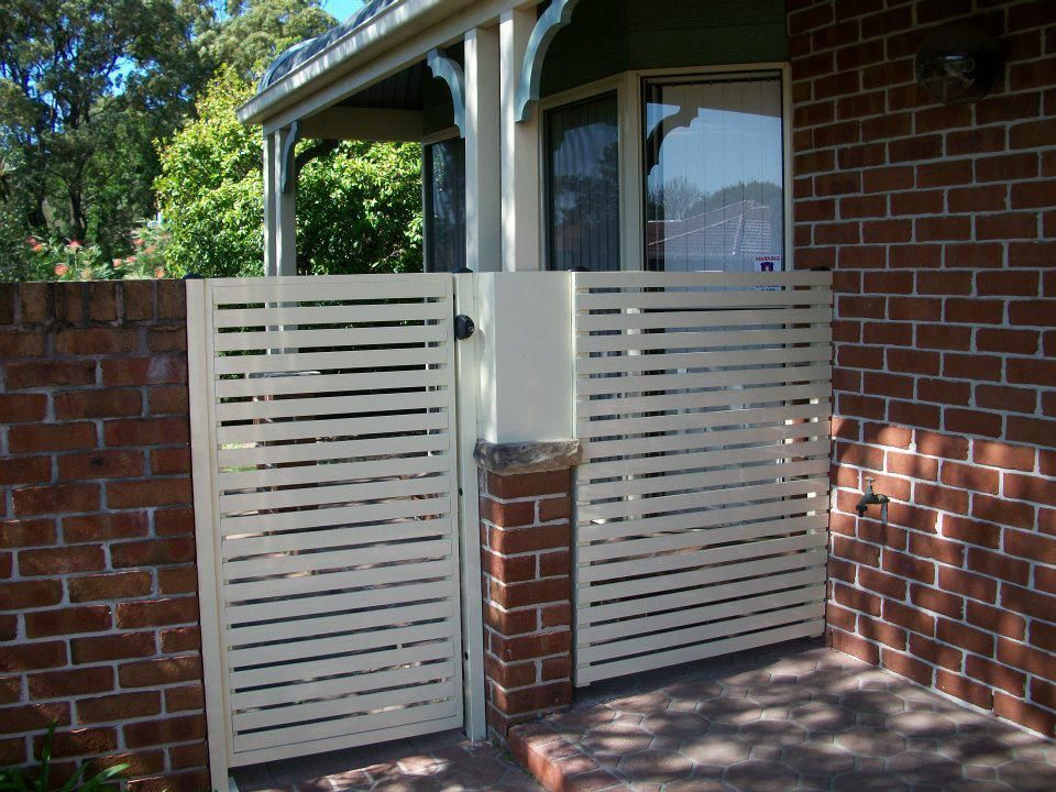 A Brick Wall with A White Gate in Front of It — Rearden Fencing Pty Ltd in Toronto, NSW