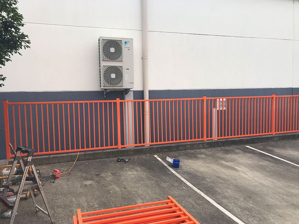 An Orange Fence is Surrounding a Parking Lot Next to a Building — Rearden Fencing Pty Ltd in Toronto, NSW