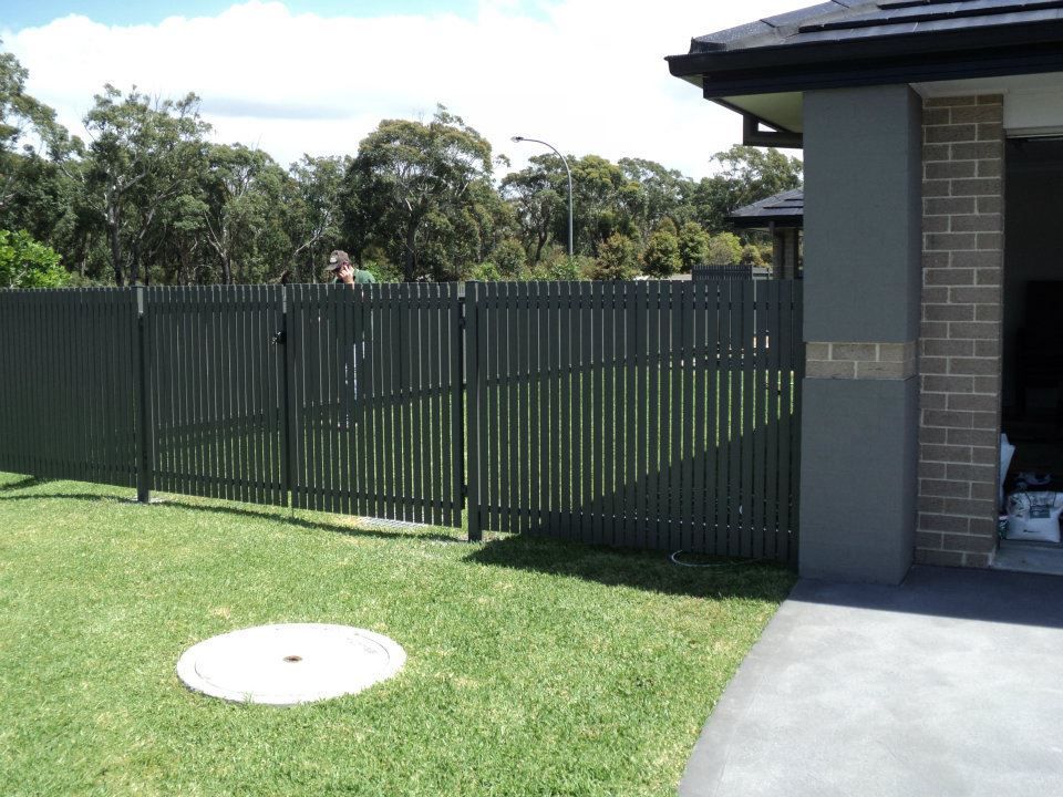A Fence Surrounds a Lush Green Yard in Front of A House — Rearden Fencing Pty Ltd in Kurri Kurri, NSW