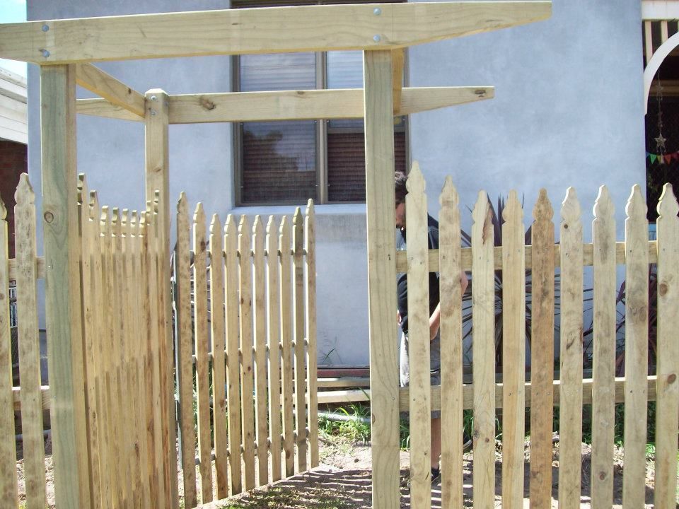 A Wooden Picket Fence with A Pergola in The Background — Rearden Fencing Pty Ltd in Toronto, NSW
