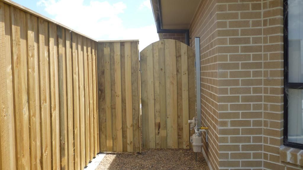 A Wooden Fence Is Next to A Brick Building — Rearden Fencing Pty Ltd in Toronto, NSW