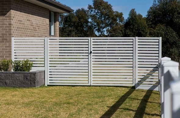 A White Fence is in Front of a Brick House — Rearden Fencing Pty Ltd in Toronto, NSW