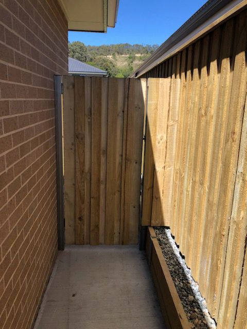A Wooden Fence Along the Side of a Brick Building — Rearden Fencing Pty Ltd in Toronto, NSW