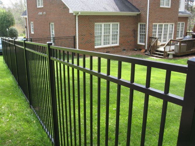 A Black Fence Surrounds a Lush Green Yard in Front of a Brick House — Rearden Fencing Pty Ltd in Toronto, NSW