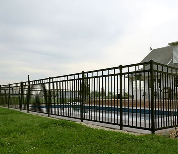 A Black Fence Surrounds a Swimming Pool in Front of a House — Rearden Fencing Pty Ltd in Toronto, NSW