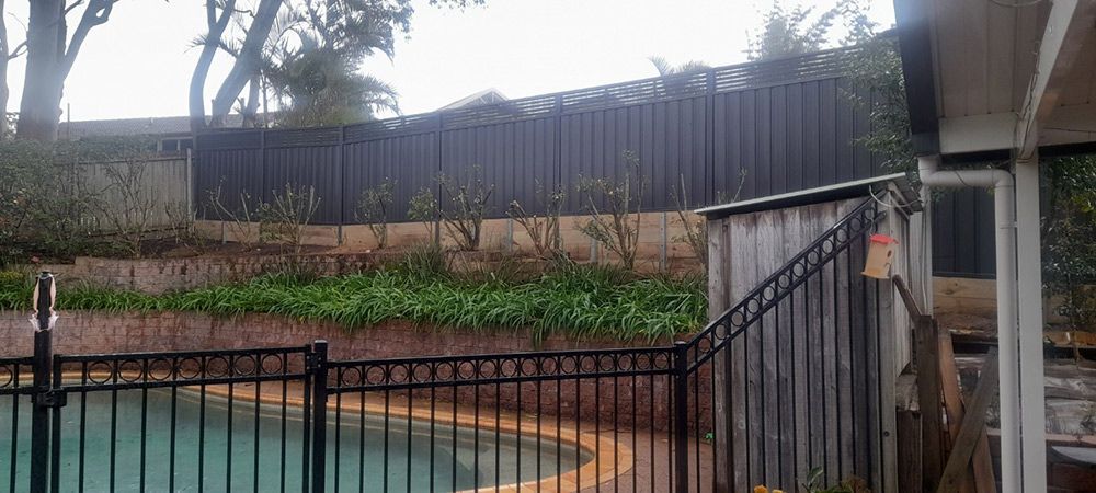 A Black Fence Surrounds a Swimming Pool in a Backyard — Rearden Fencing Pty Ltd in Toronto, NSW