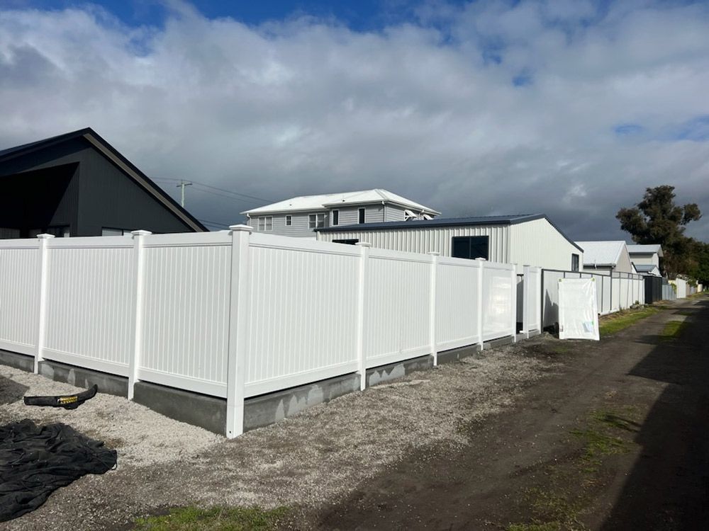 A White Fence Surrounds a Dirt Road in Front of a House — Rearden Fencing Pty Ltd in Toronto, NSW