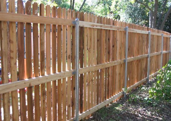 A Wooden Fence With Metal Posts is Surrounded by Trees — Rearden Fencing Pty Ltd in Toronto, NSW
