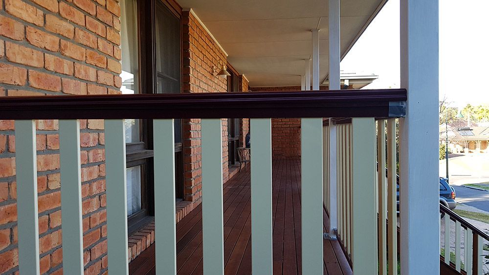A Brick Building With a White Railing and a Wooden Deck — Rearden Fencing Pty Ltd in Toronto, NSW