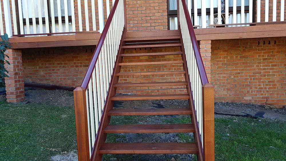 A Wooden Staircase Leading Up to a Deck With a White Railing — Rearden Fencing Pty Ltd in Toronto, NSW
