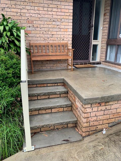 A Wooden Bench is Sitting on a Porch Next to a Brick Wall — Rearden Fencing Pty Ltd in Toronto, NSW