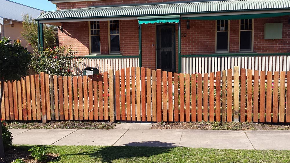 A Brick House With a Wooden Fence in Front of It — Rearden Fencing Pty Ltd in Toronto, NSW