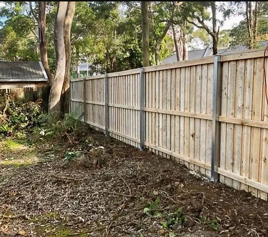 A Wooden Fence is Surrounded by Trees in a Yard — Rearden Fencing Pty Ltd in Toronto, NSW