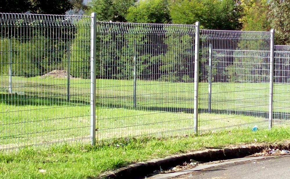 A Wire Fence Surrounds a Grassy Field Next to a Road — Rearden Fencing Pty Ltd in Toronto, NSW