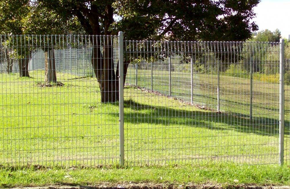 A Wire Fence Surrounds a Grassy Field With Trees in the Background — Rearden Fencing Pty Ltd in Toronto, NSW