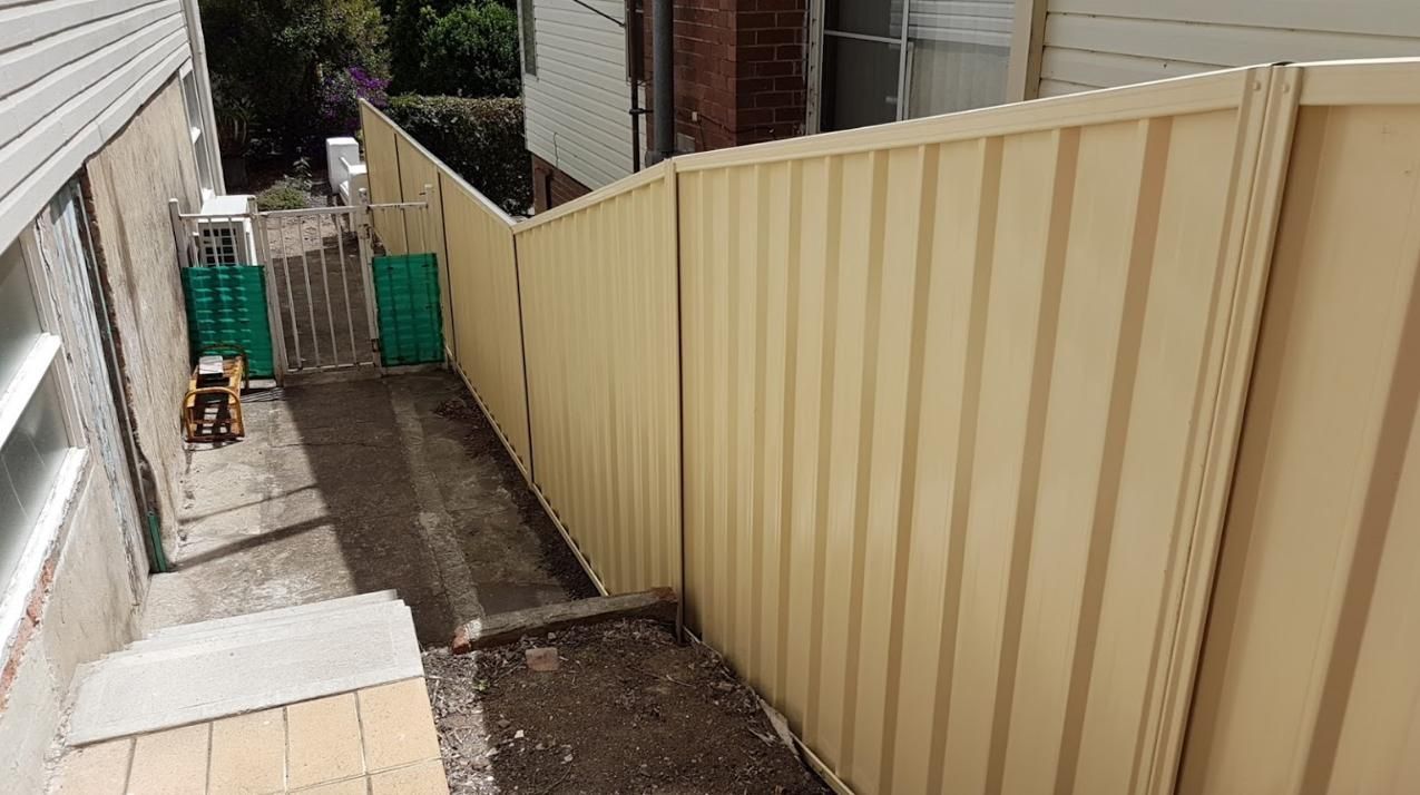A Beige Fence Is Sitting Next to A House — Rearden Fencing Pty Ltd in Rutherford, NSW