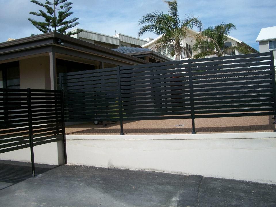 A Black Fence Surrounds a House with Palm Trees in The Background — Rearden Fencing Pty Ltd in Cessnock, NSW