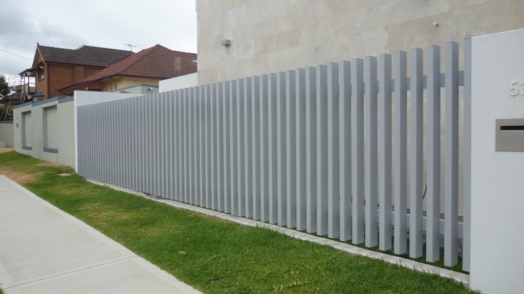 A White Fence Surrounds a Lush Green Yard in Front of A House — Rearden Fencing Pty Ltd in Toronto, NSW