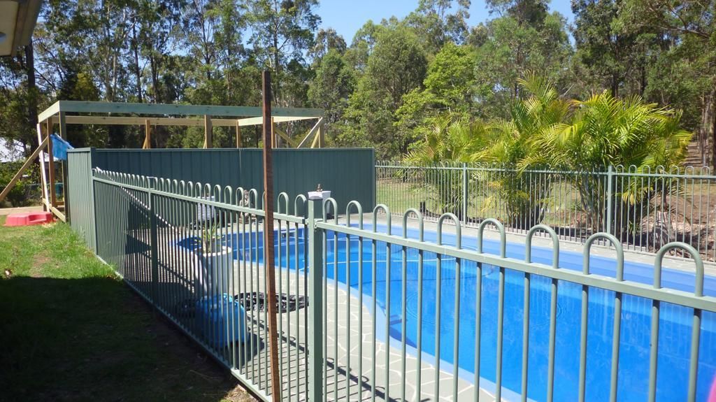 A Fence Surrounds a Swimming Pool with Trees in The Background — Rearden Fencing Pty Ltd in Toronto, NSW