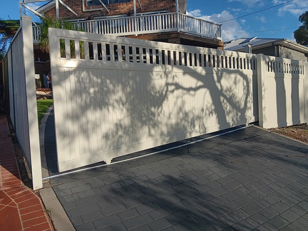 A White Fence is Surrounding a Driveway in Front of a House — Rearden Fencing Pty Ltd in Toronto, NSW