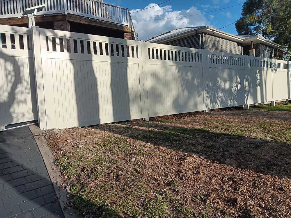 A White Fence is Surrounding a Grassy Field in Front of a House — Rearden Fencing Pty Ltd in Toronto, NSW