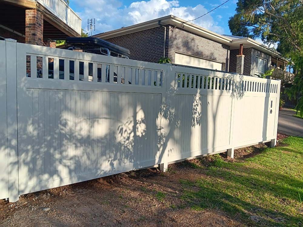 A White Fence is Sitting in Front of a House — Rearden Fencing Pty Ltd in Toronto, NSW