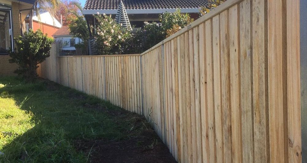 A Wooden Fence Surrounds a Grassy Yard in Front of a House — Rearden Fencing Pty Ltd in Toronto, NSW