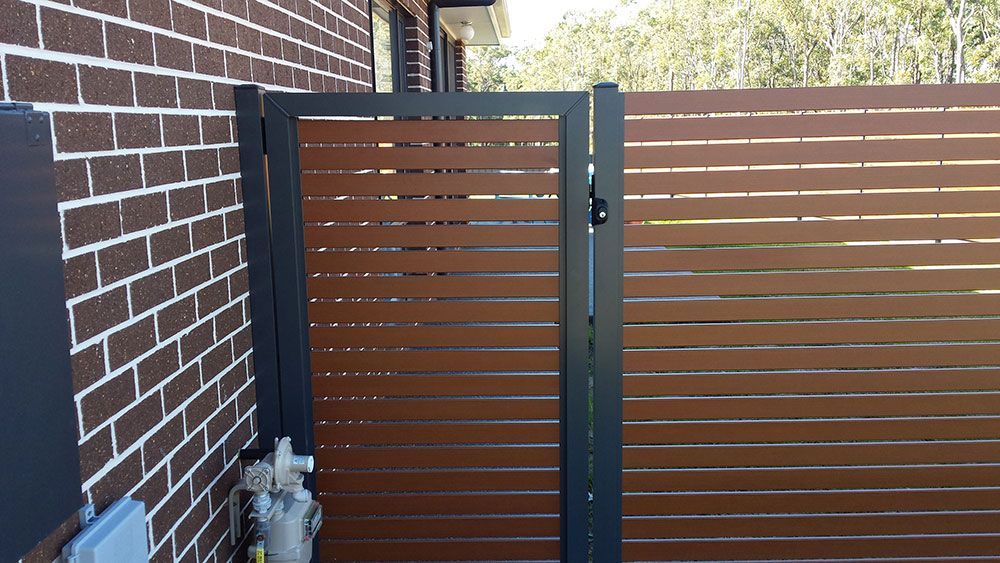 A Wooden Fence With a Gate in Front of a Brick Building — Rearden Fencing Pty Ltd in Toronto, NSW