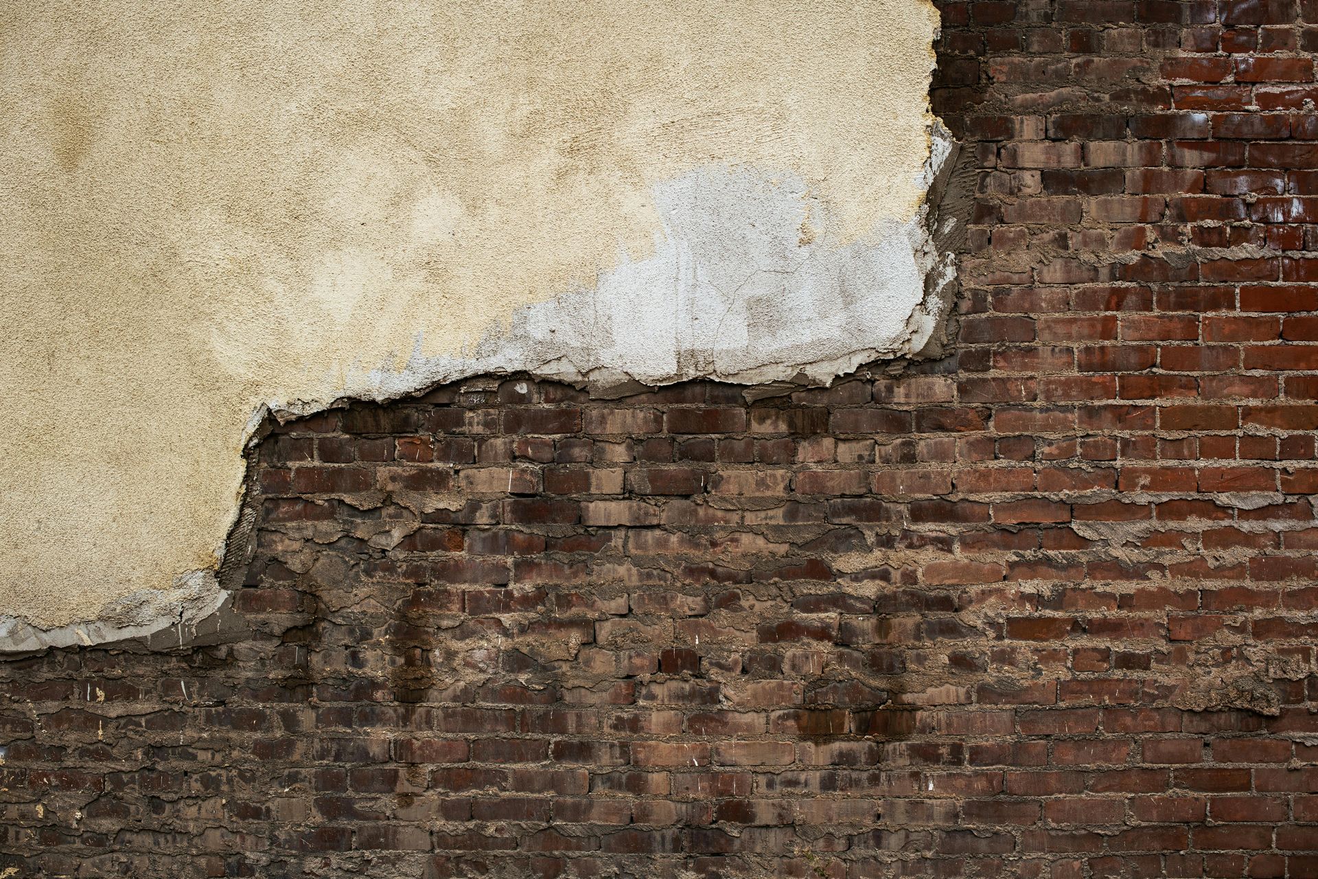 Exposed brick wall with peeling beige plaster.