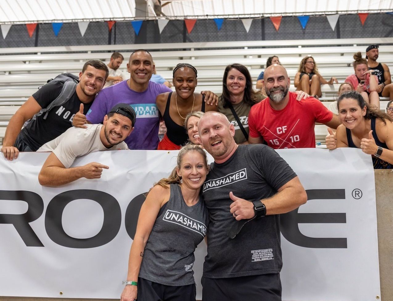Group of people smiling, posing behind a Rogue banner. Some give thumbs up. Indoor setting.