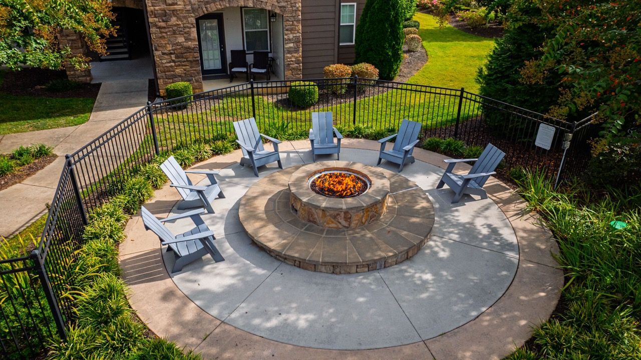 Circular stone fire pit with blue Adirondack chairs arranged around a seating circle in a landscaped apartment courtyard.