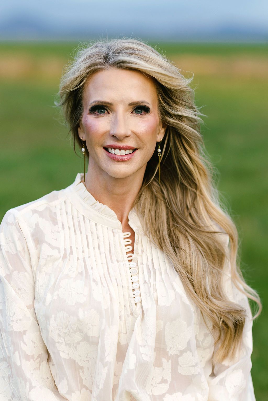 Smiling woman in a satin blouse and white pants seated on a white bench indoors