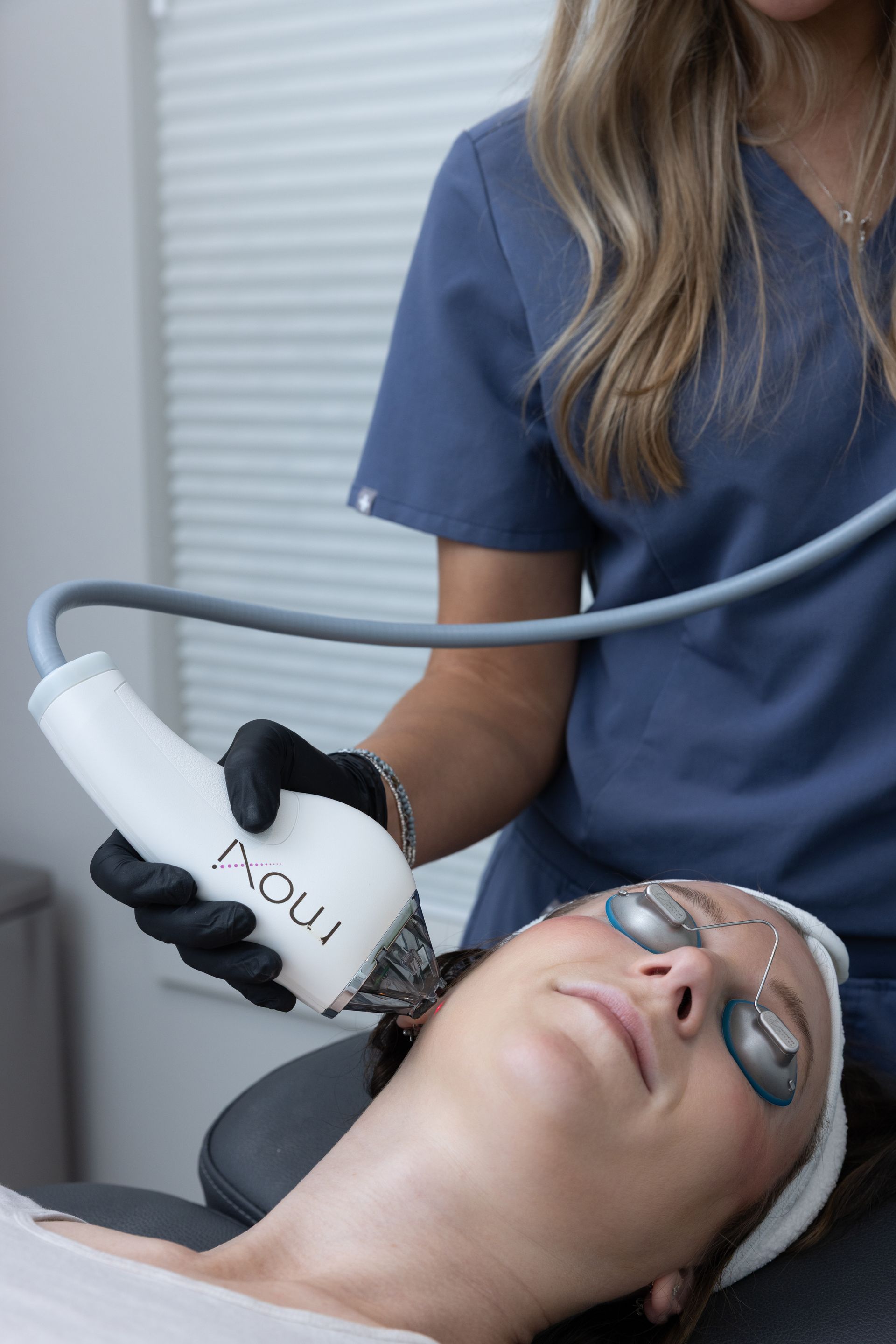 Facial treatment with a handheld device on a reclining client in a spa room