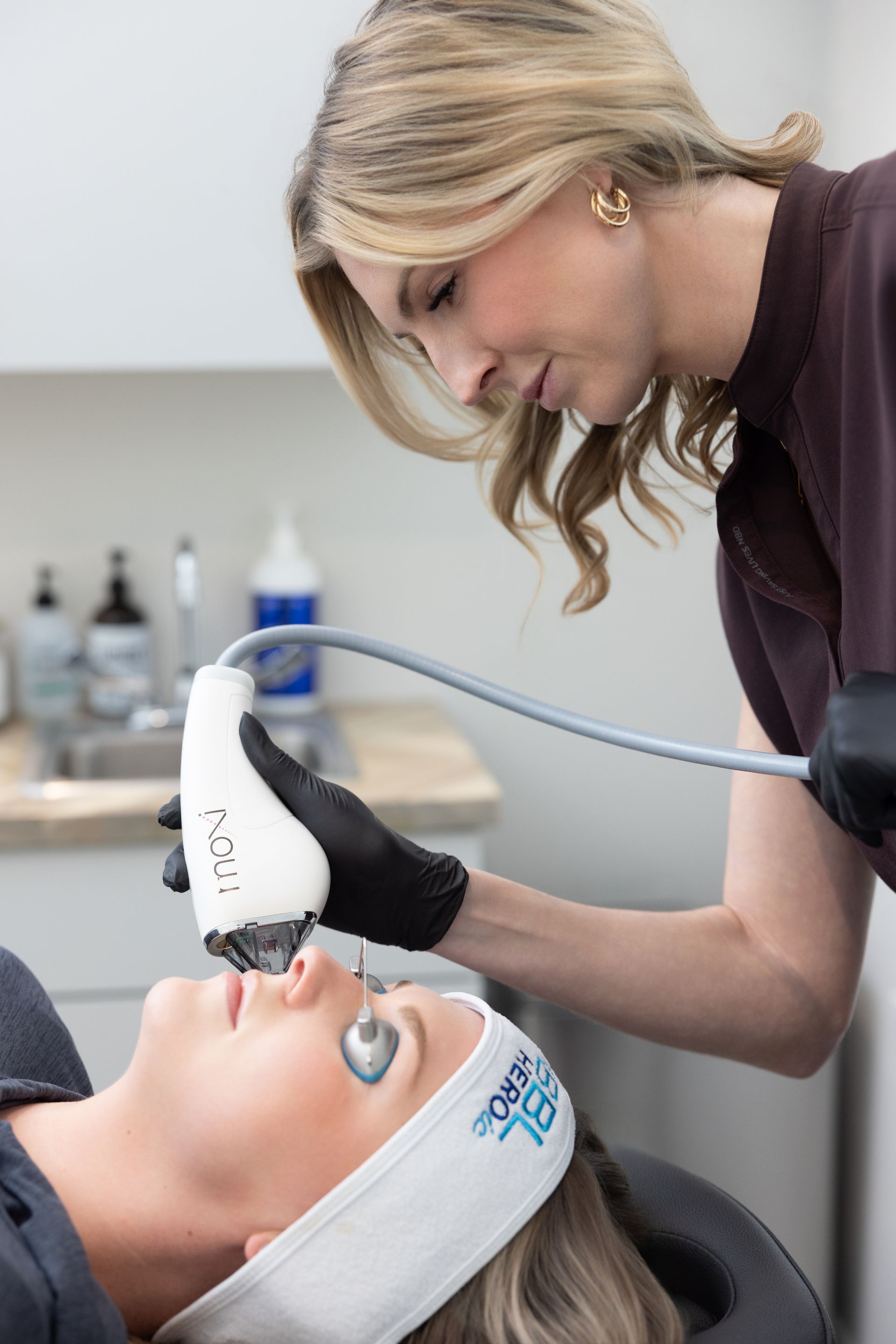 Esthetician using a handheld facial device on a client lying in a treatment chair