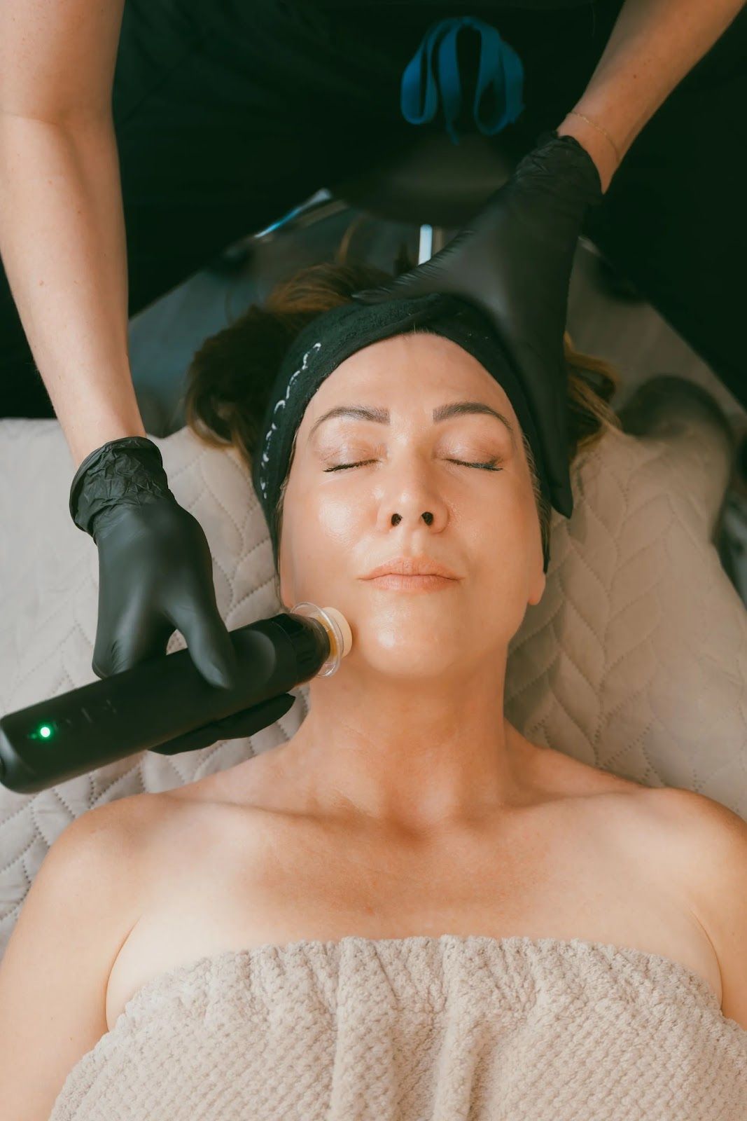 A person receives a professional facial treatment using a handheld device while lying on a spa table.