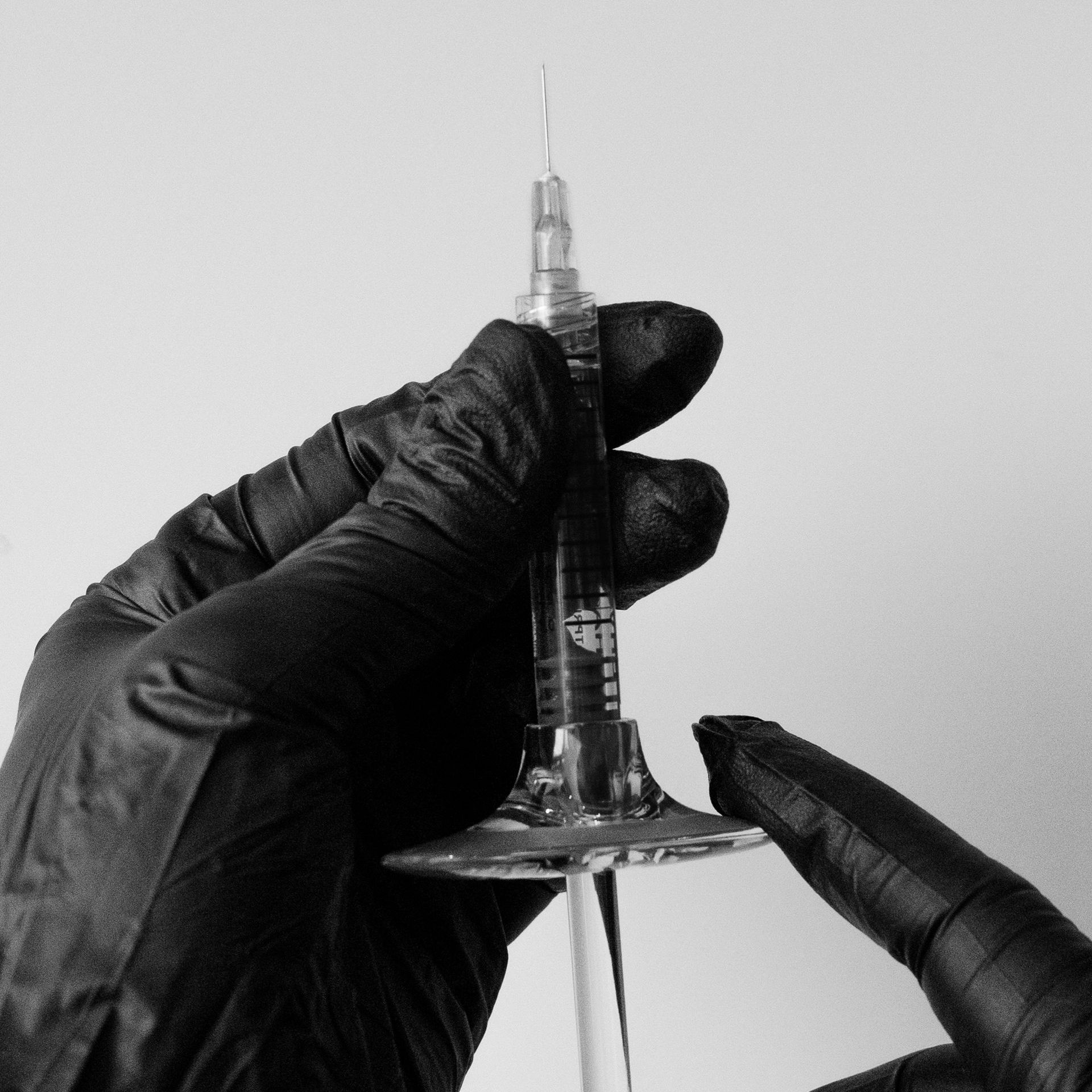 A person wearing black gloves is holding a glass with a syringe in it.