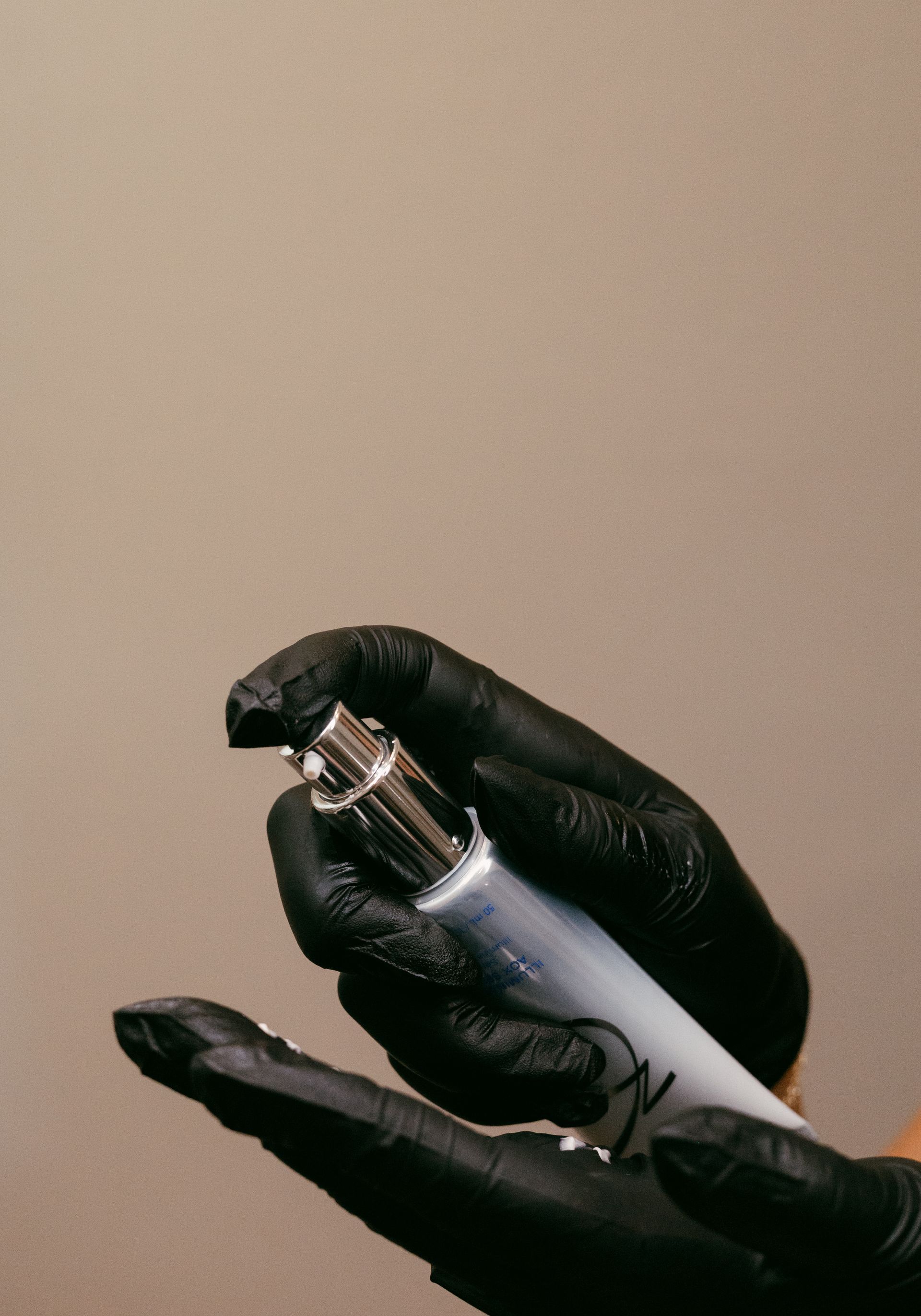 A person wearing black gloves is holding a bottle of lotion.