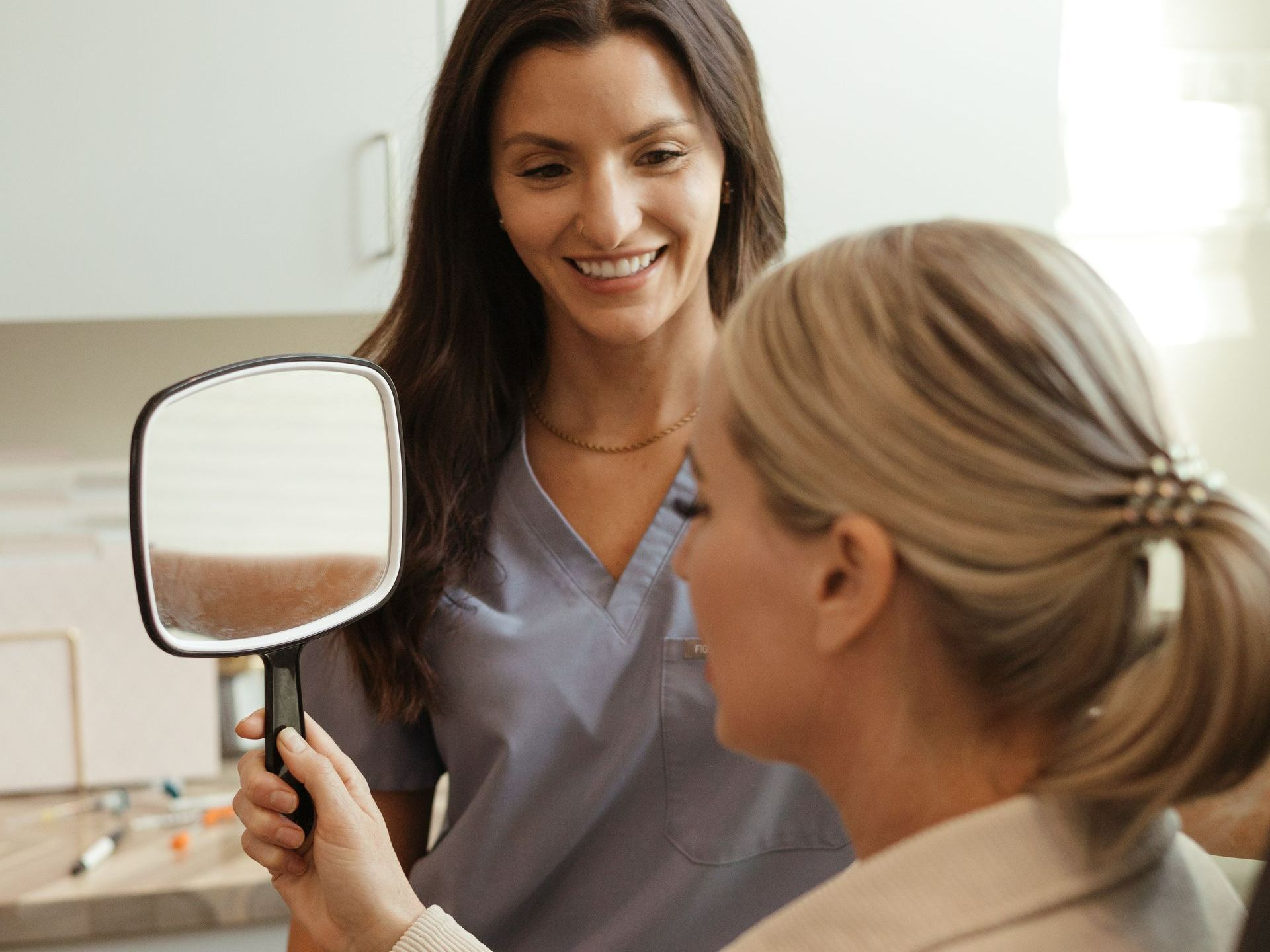 A woman is looking at herself in a mirror while sitting in a chair.