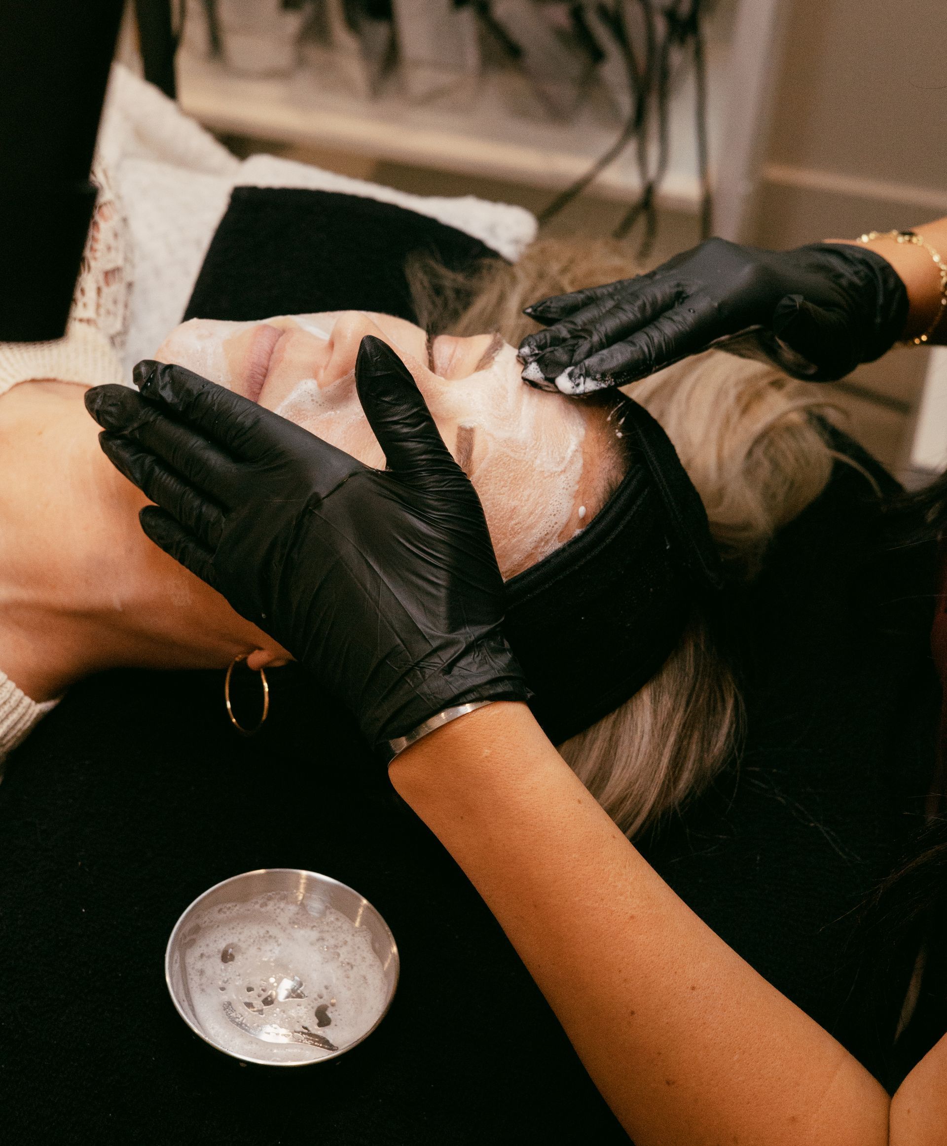 Woman receiving facial treatment, blue-gloved hands holding applicator, clinic setting.