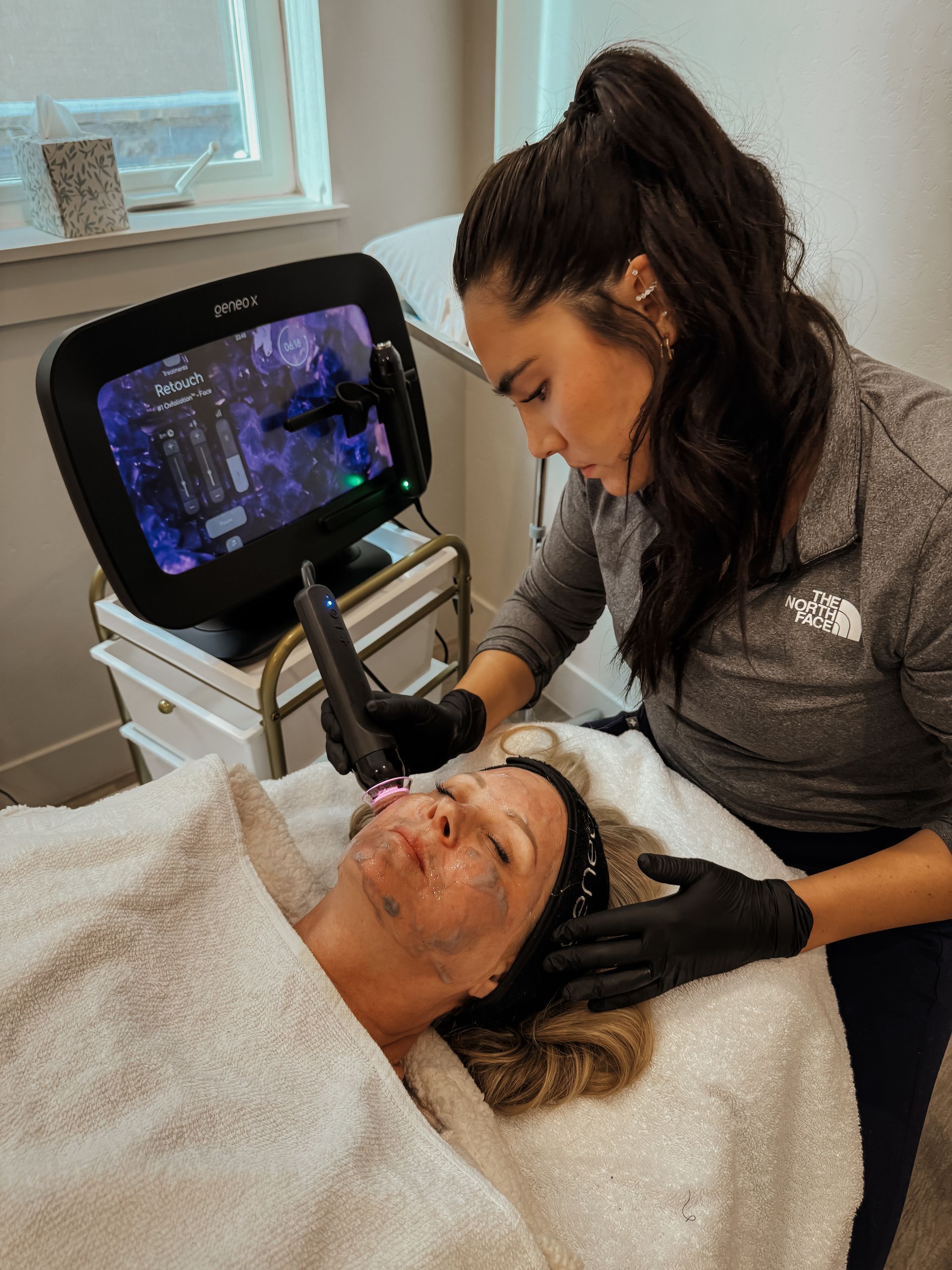 Facial treatment in progress with clinician using a handheld device on a reclined client in a spa room