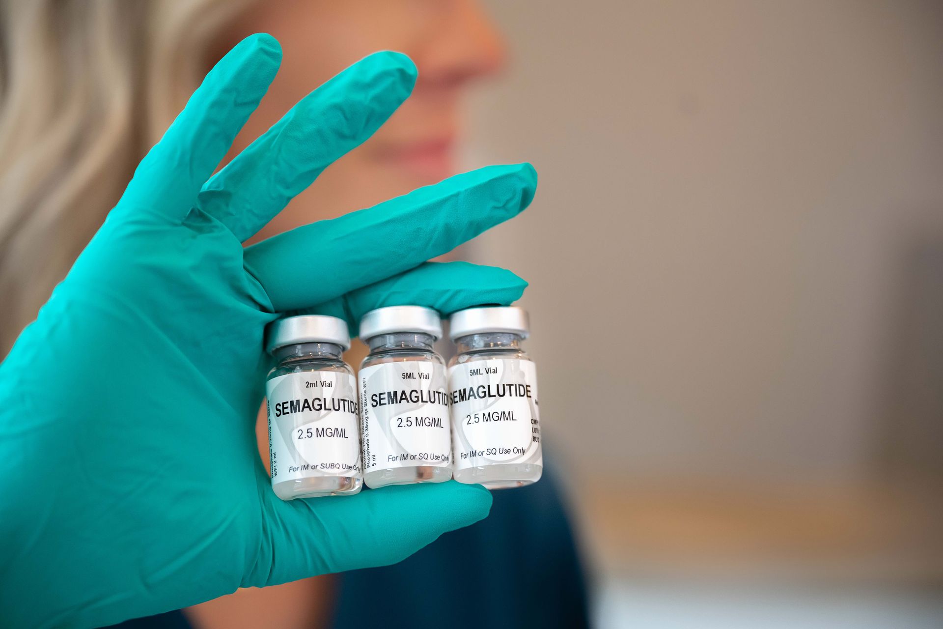 a person wearing a green glove is holding three bottles of medication .