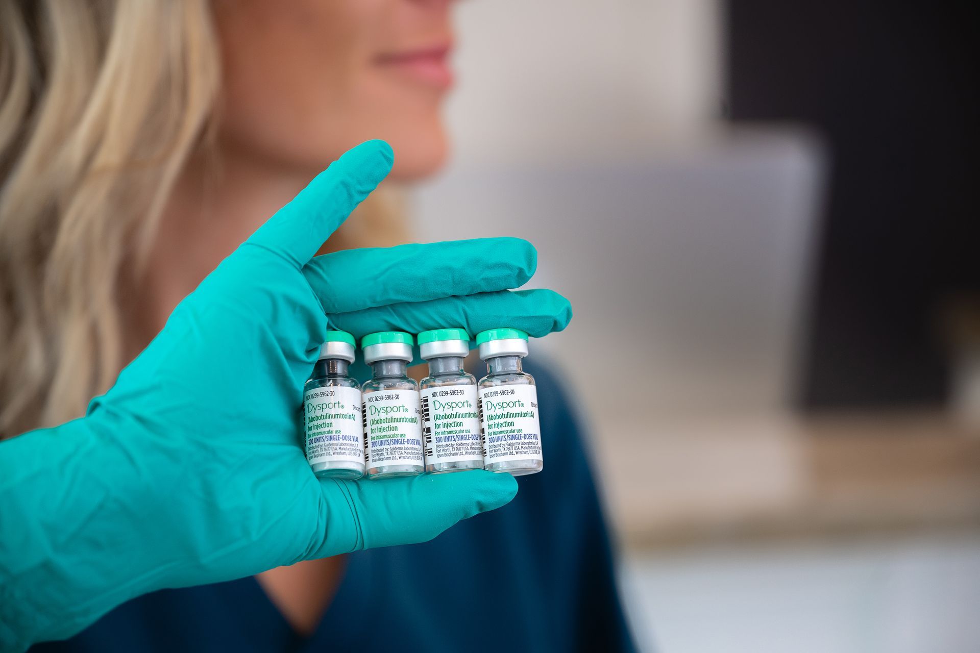 Gloved hand holding four small vaccine vials in front of a blurred person